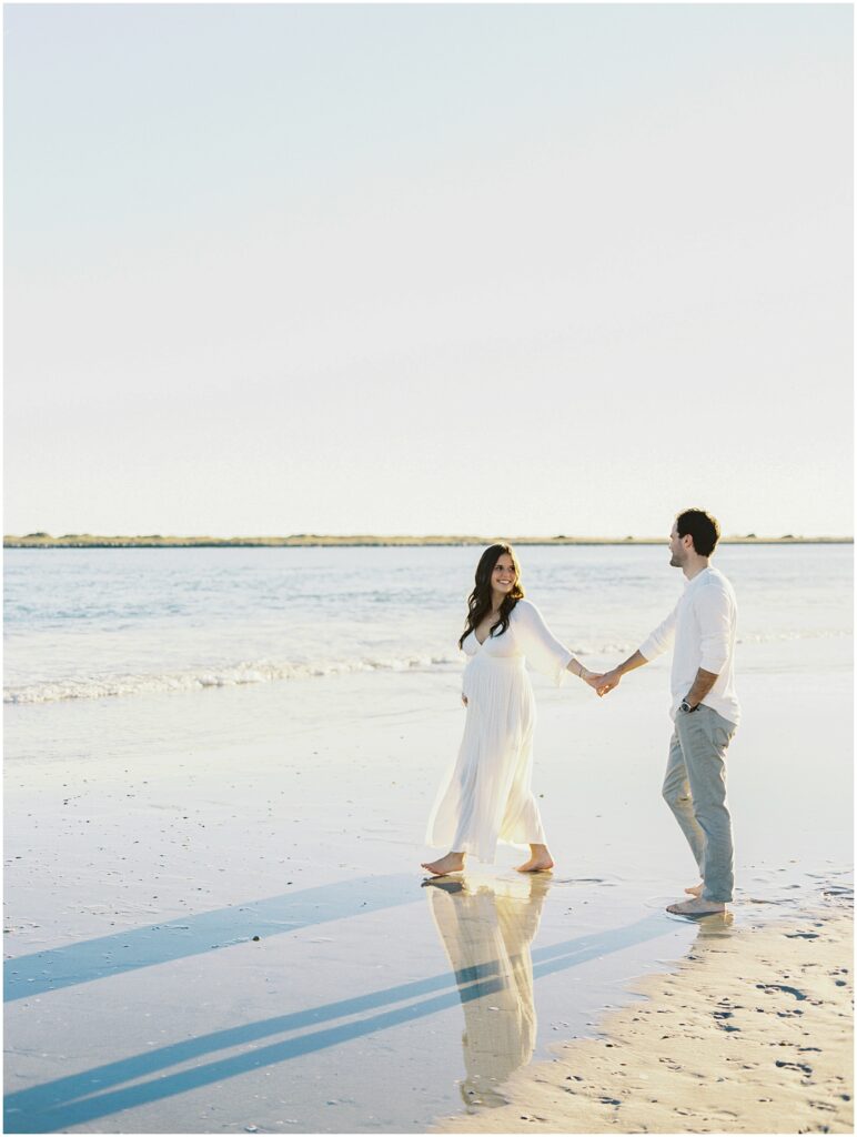 Expecting parents walking along the shoreline during a Wrightsville Beach maternity session