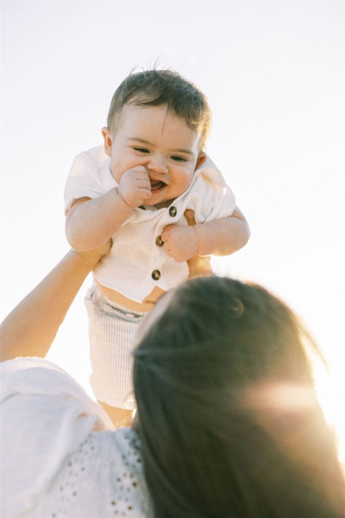 mom throwing baby up in the air on the beach in Wilmington