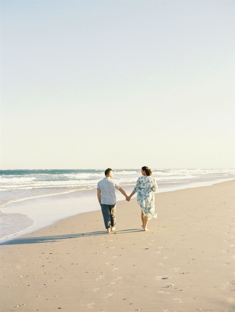 mom and dad holding hands and walking away during maternity photos on Topsail beach